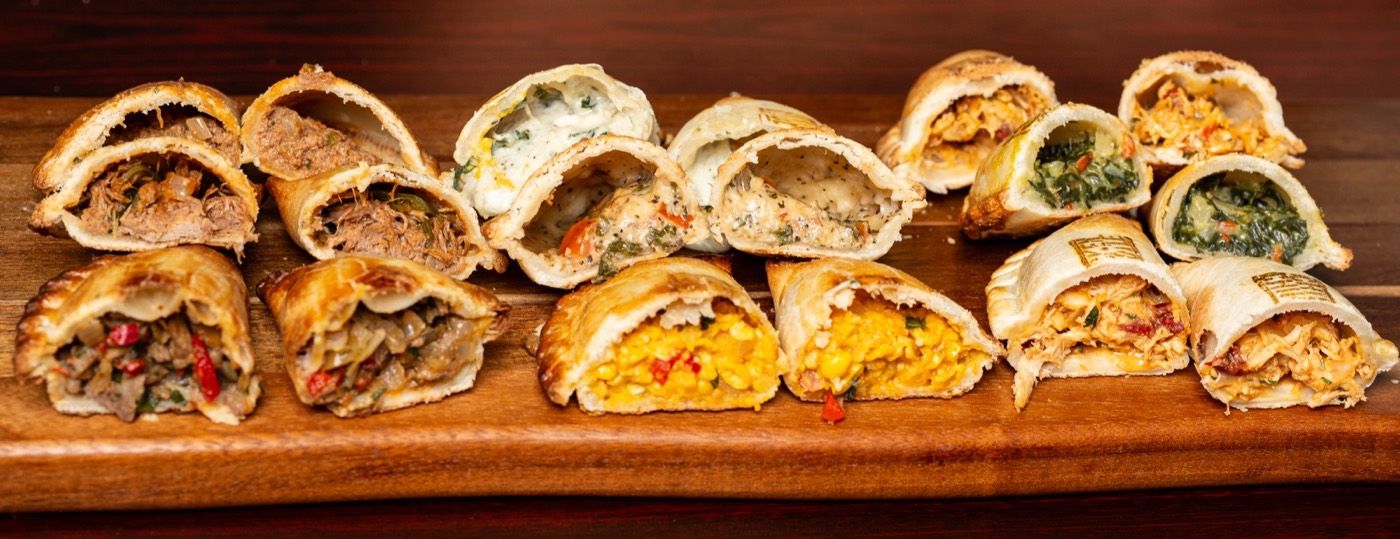 A long board of empanadas cut open, with dipping sauces