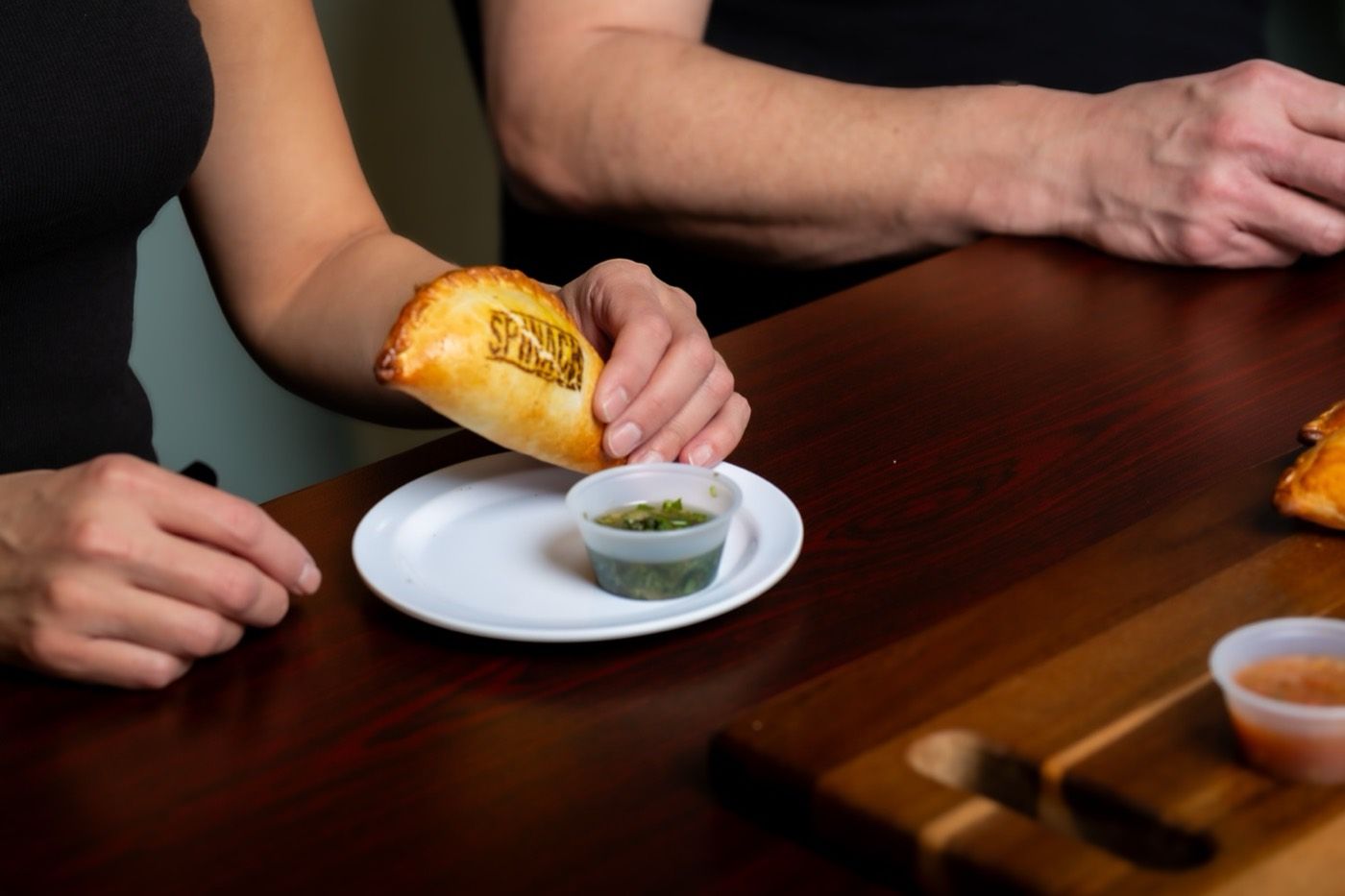 A hand dipping an empanada into chimichurri